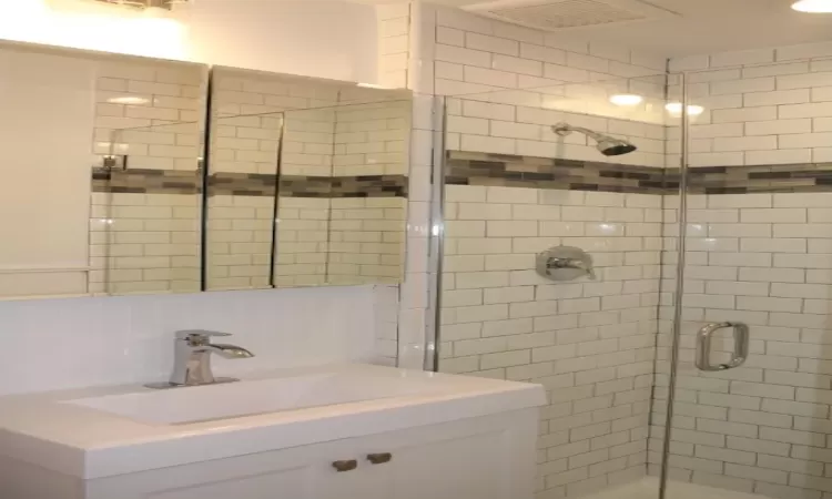 Full bathroom with a sink, visible vents, tasteful backsplash, and a shower stall