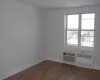 Unfurnished room featuring a wall mounted air conditioner, baseboards, radiator, and wood finished floors