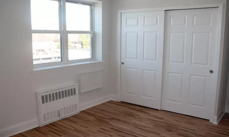 Unfurnished bedroom featuring radiator, wood finished floors, and baseboards