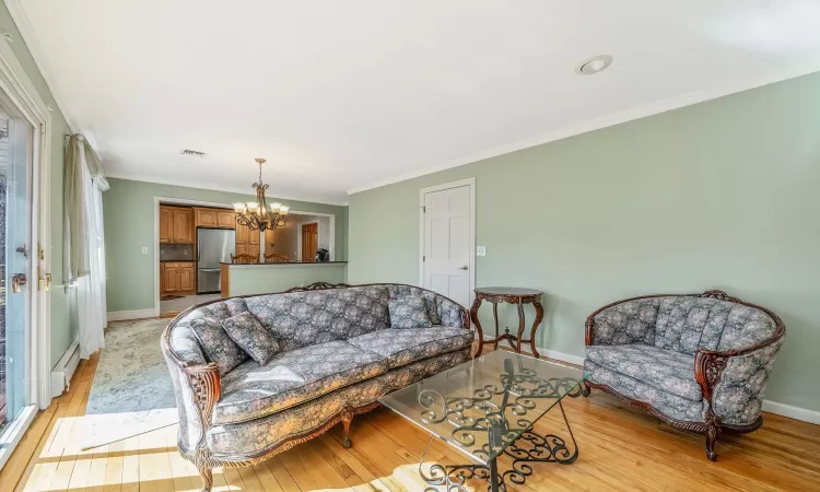 Living room with ornamental molding, an inviting chandelier, light wood finished floors, a baseboard radiator, and baseboards