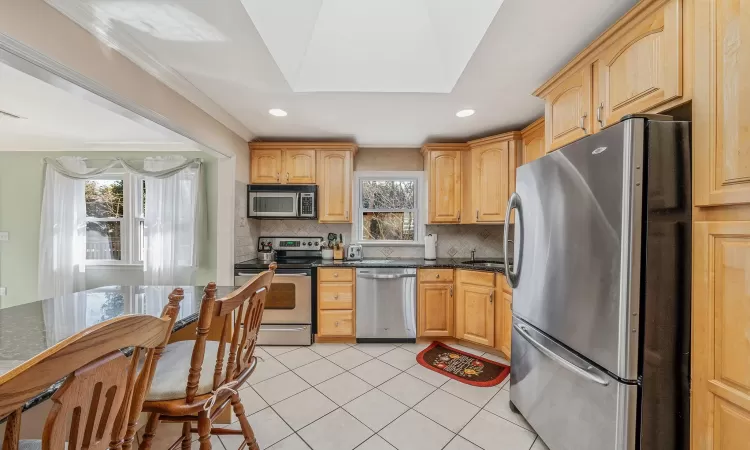 Kitchen with light tile patterned floors, appliances with stainless steel finishes, tasteful backsplash, and light brown cabinetry