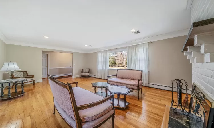 Living room with visible vents, a brick fireplace, light wood-type flooring, and ornamental molding