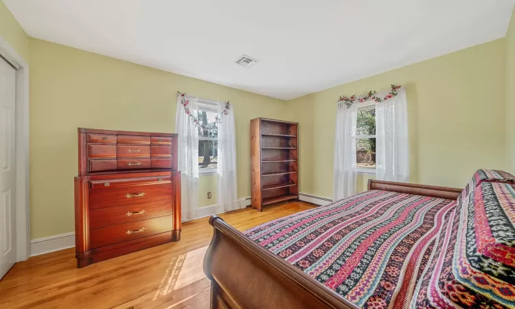 Bedroom featuring visible vents, baseboards, a baseboard heating unit, and light wood-style flooring