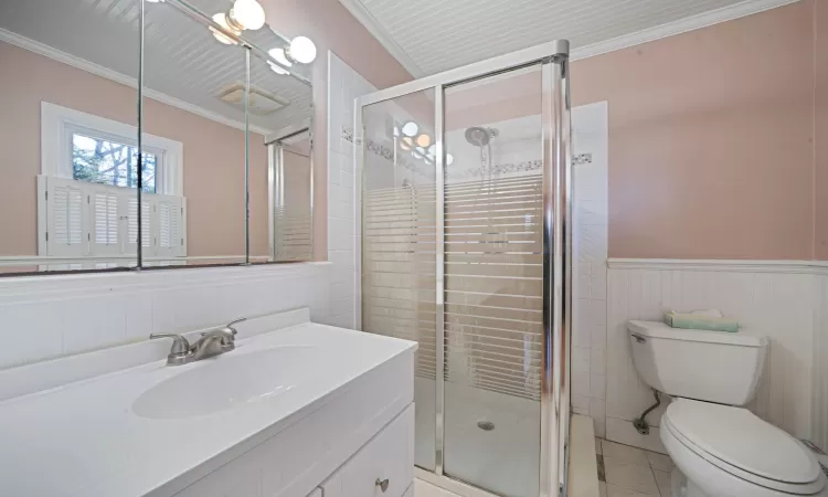 Bathroom with crown molding, toilet, a stall shower, and wainscoting