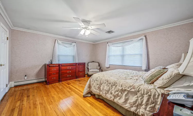 Bedroom with visible vents, a baseboard heating unit, ornamental molding, hardwood / wood-style flooring, and a ceiling fan