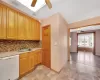 Kitchen with a sink, backsplash, stone tile flooring, white dishwasher, and baseboards