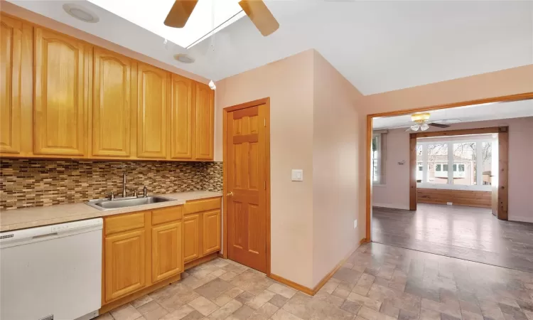 Kitchen with a sink, backsplash, stone tile flooring, white dishwasher, and baseboards