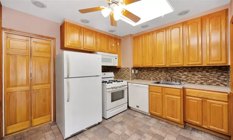 Kitchen featuring stone tile flooring, white appliances, light countertops, and a sink