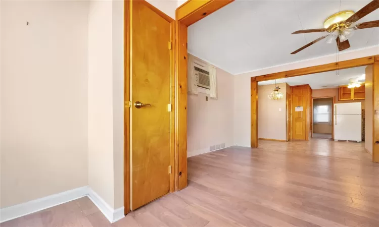 Empty room featuring visible vents, a wall unit AC, light wood-style floors, baseboards, and ceiling fan