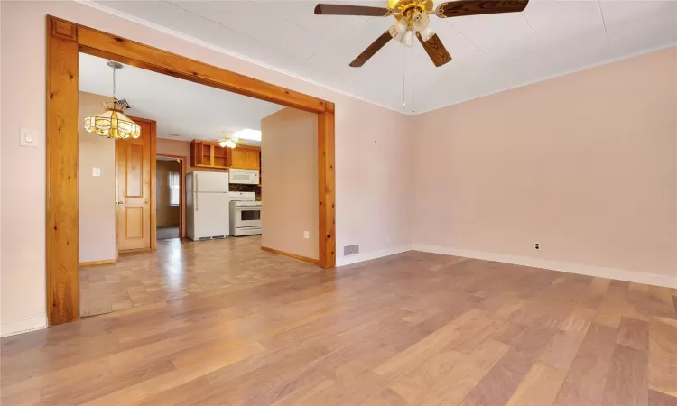 Unfurnished living room featuring light wood finished floors, visible vents, crown molding, baseboards, and a ceiling fan