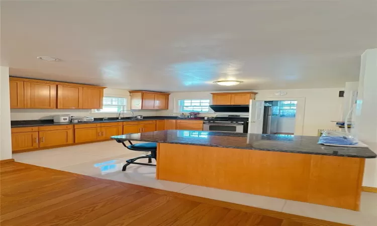 Kitchen with a sink, dark stone counters, stainless steel range with gas stovetop, and light wood finished floors