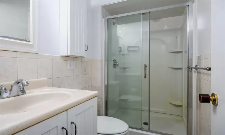 Bathroom featuring vanity, toilet, tile walls, and a shower stall