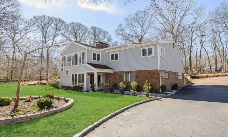 View of front facade featuring aphalt driveway, brick siding, a chimney, and a front lawn