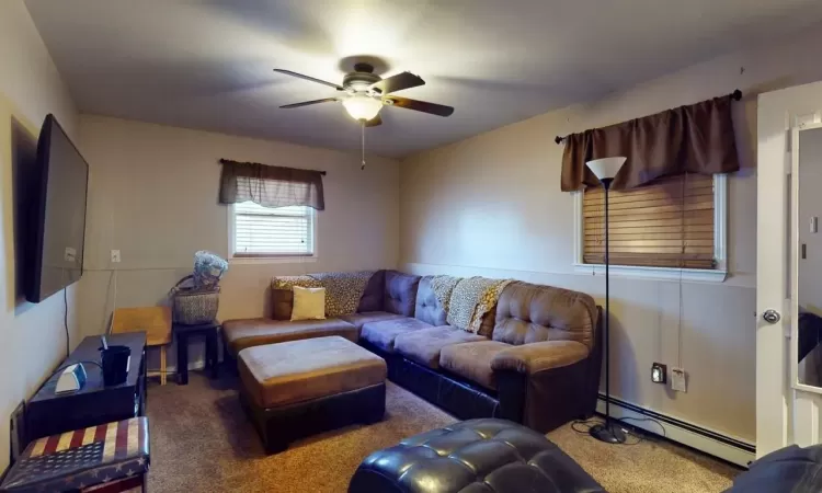 Carpeted living room featuring a ceiling fan and baseboard heating