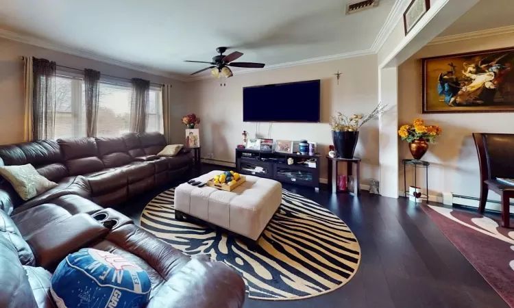 Living area featuring a baseboard radiator, wood finished floors, visible vents, and ornamental molding