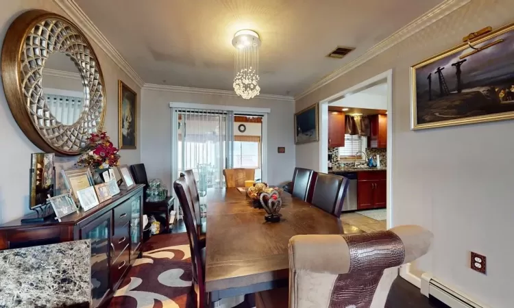 Dining area with visible vents, baseboard heating, ornamental molding, and a chandelier