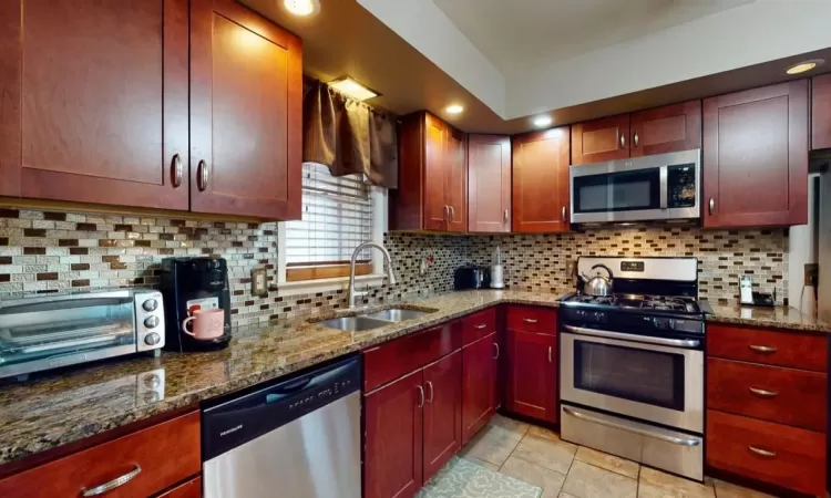 Kitchen featuring a sink, backsplash, stainless steel appliances, dark stone counters, and a toaster