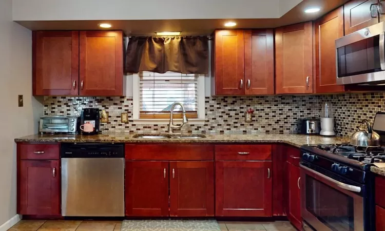 Kitchen with backsplash, stainless steel appliances, dark stone counters, and a sink