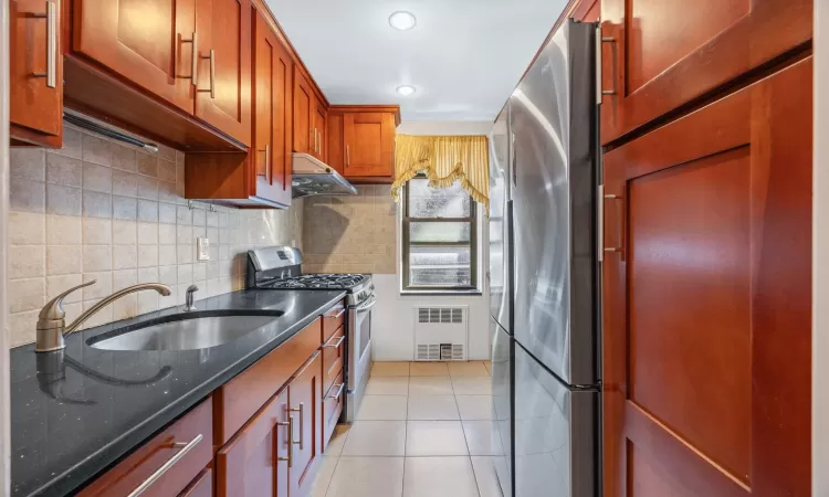 Kitchen featuring under cabinet range hood, a sink, tasteful backsplash, appliances with stainless steel finishes, and light tile patterned floors