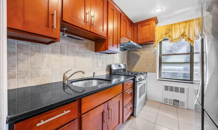 Kitchen featuring radiator, under cabinet range hood, gas range, light tile patterned floors, and a sink