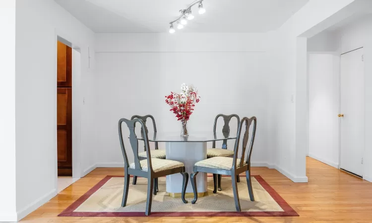 Dining area featuring light wood-style flooring, rail lighting, and baseboards