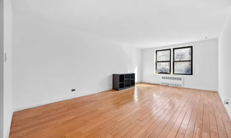 Unfurnished living room with radiator heating unit, baseboards, and light wood-type flooring