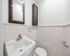 Bathroom featuring wainscoting, toilet, tile walls, and a sink