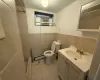 Bathroom with toilet, tile walls, tile patterned flooring, tiled shower, and baseboard heating