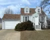 Cape cod house with an attached garage, roof with shingles, concrete driveway, and a chimney