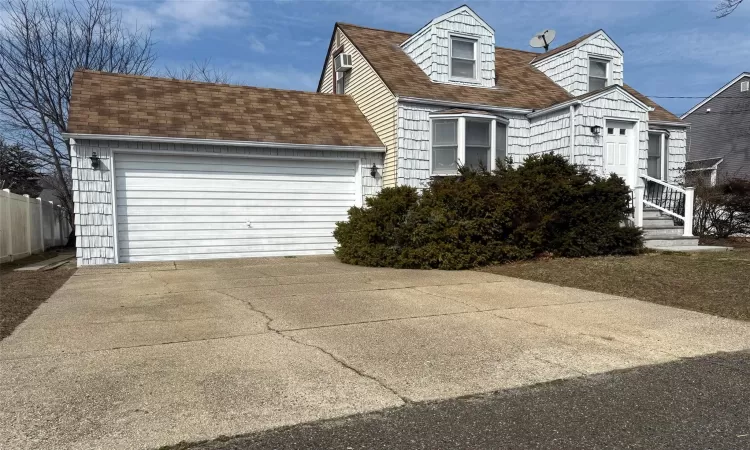 New england style home with an attached garage, roof with shingles, driveway, and fence