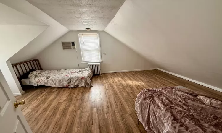 Bedroom with radiator, baseboards, lofted ceiling, wood finished floors, and a textured ceiling