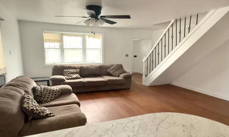 Living room with stairway, ceiling fan, baseboards, and wood finished floors