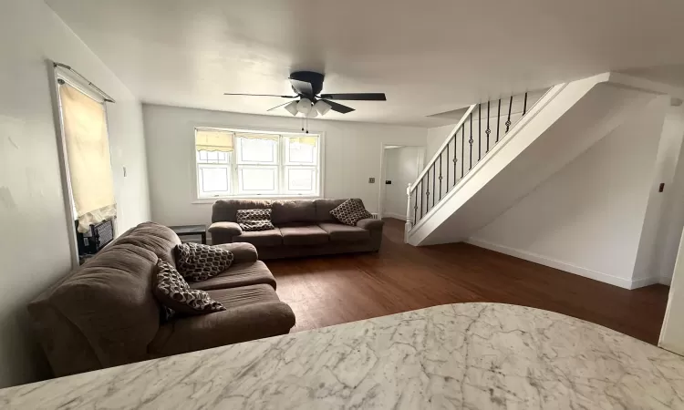 Living room featuring ceiling fan, stairway, baseboards, and wood finished floors