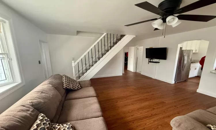 Living area with a ceiling fan, stairway, dark wood-style floors, and baseboards