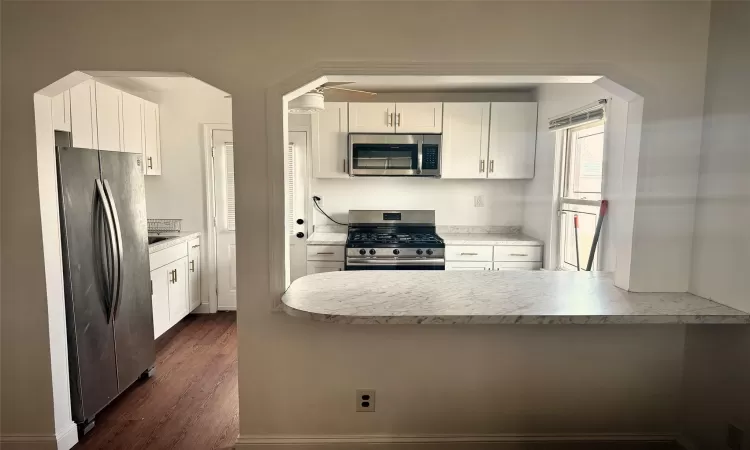 Kitchen with arched walkways, appliances with stainless steel finishes, white cabinets, light countertops, and dark wood-style flooring