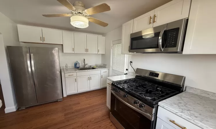 Kitchen featuring a sink, dark wood finished floors, white cabinetry, appliances with stainless steel finishes, and light stone countertops