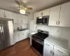 Kitchen featuring dark wood-type flooring, a sink, white cabinetry, stainless steel appliances, and light stone countertops