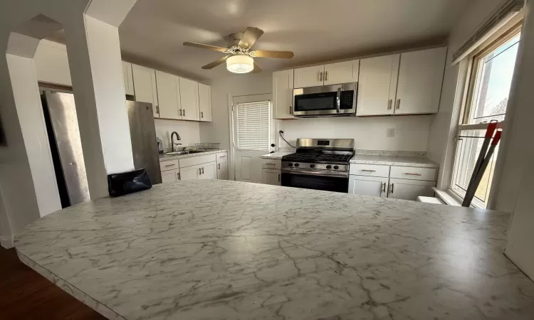 Kitchen featuring a ceiling fan, a sink, appliances with stainless steel finishes, white cabinets, and light countertops