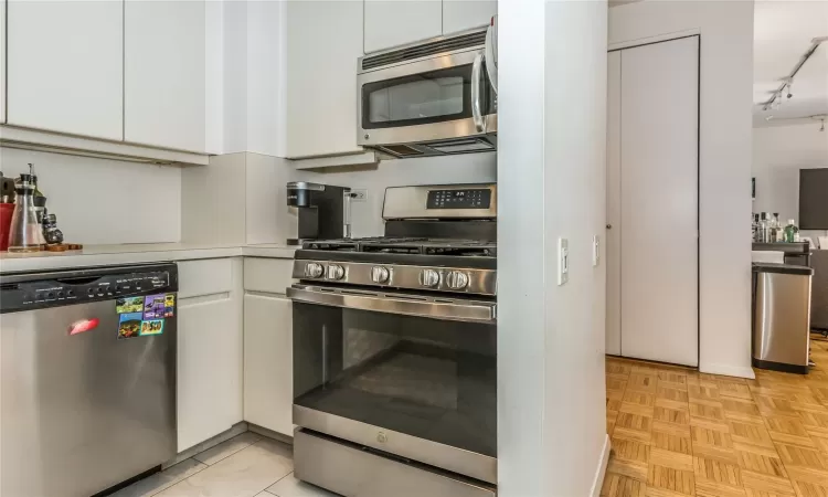 Kitchen featuring appliances with stainless steel finishes, white cabinets, light countertops, and track lighting