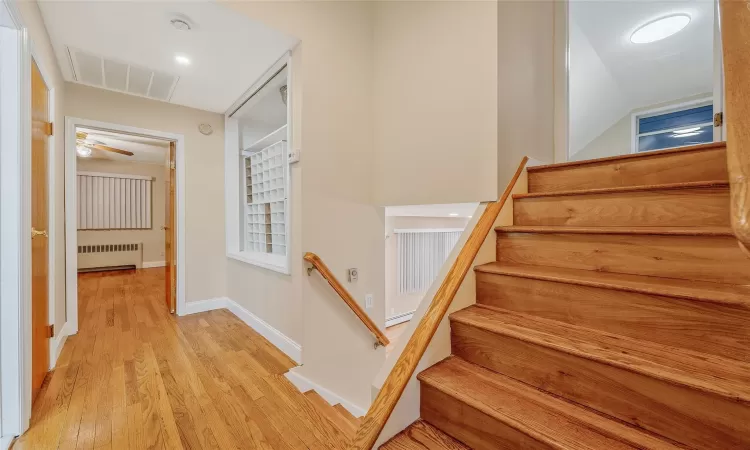 Stairway featuring visible vents, radiator heating unit, baseboards, and wood finished floors