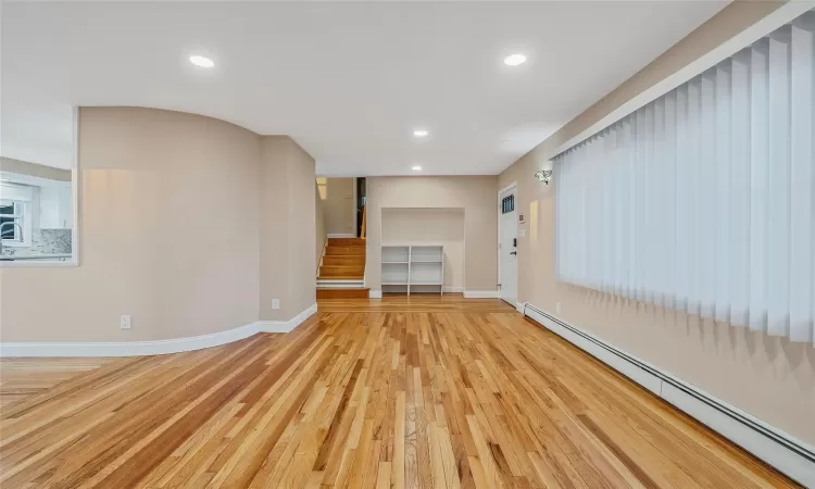 Unfurnished living room featuring stairway, baseboards, baseboard heating, and light wood-style flooring