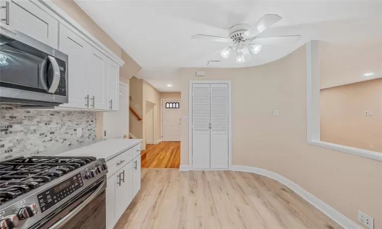 Kitchen with light wood-style floors, tasteful backsplash, appliances with stainless steel finishes, and baseboards