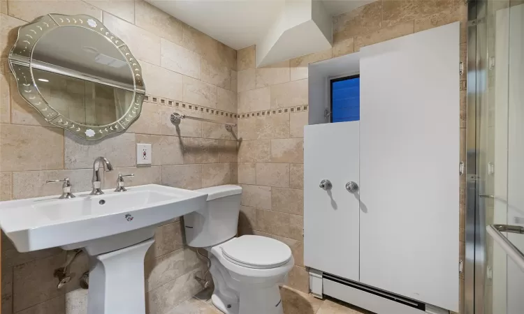 Full bath featuring a shower with shower door, a baseboard radiator, toilet, and tile walls