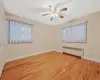 Empty room featuring a wealth of natural light, light wood-style flooring, radiator heating unit, and baseboards