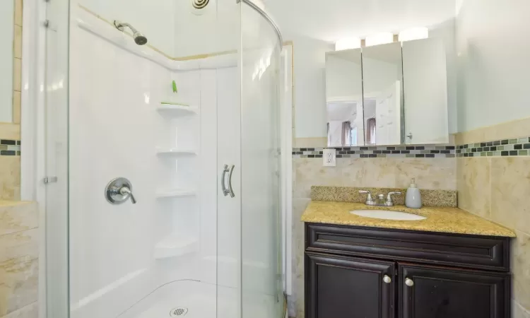 Bathroom featuring a stall shower, vanity, and tile walls