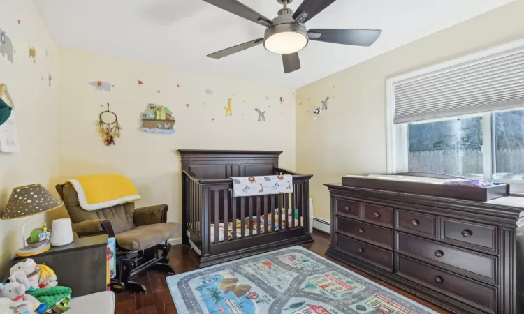 Bedroom featuring a baseboard heating unit, a nursery area, wood finished floors, and a ceiling fan