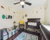 Bedroom with a nursery area, a ceiling fan, baseboards, and wood finished floors