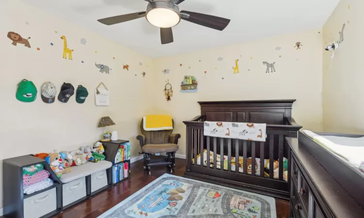 Bedroom with a nursery area, a ceiling fan, baseboards, and wood finished floors