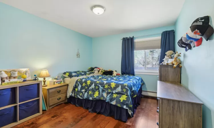 Bedroom with dark wood-style floors and a baseboard radiator