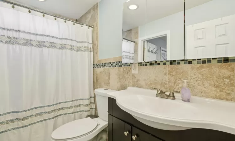 Bathroom featuring toilet, vanity, tile walls, and a shower with curtain